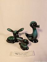Lot containing three vintage Blue Mountain Pottery ceramic figurines: duck, rabbit, and small deer/gazelle animal, black and turquoise-green glaze, displayed upright.