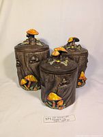 Three vintage ceramic Treasure Craft canisters with warm orange mushroom decorations, varying sizes with lids, shown against white background