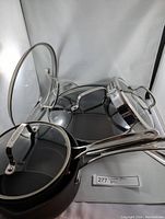 Multiple Cuisinart pans and pots with glass lids displayed, showing stainless steel handles and lids with vent holes.