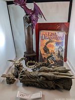 Photo showing the dragon-shaped incense burner in front with a large purple dragon statue behind, two books, and several small figurines arranged around.