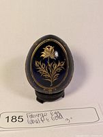 Front view showing gold etched floral design on cobalt blue egg with stand and handwritten label.