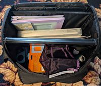 Top open view of bag showing scrapbook binders, paper hole punches, and craft materials inside