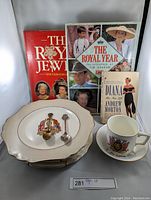 Photo showing books including The Royal Jewels, The Royal Year 1984, Diana Her True Story, royal-themed plates, souvenir spoons, and mugs.