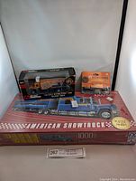 Photo showing the sealed Schmidt 1000-piece puzzle box featuring an image of a blue American show truck, and two boxes containing Ertl diecast trucks on top of the puzzle box.