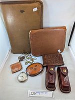 Full view of all vintage leather items including folder, zippered case, card holder, leather holders, pocket watch, magnifying glass