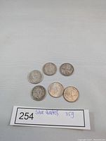 Top-down photo of six silver Canadian quarters arranged on cloth with lot card showing 'silver quarters 35g'.