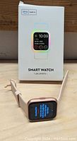 Photo of the boxed smart watch standing upright with the watch displayed in front on a wooden surface showing the watch screen on.