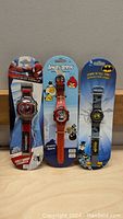 Photo of three themed kids wrist watches still on their retail packaging, featuring Spider-Man, Angry Birds, and Batman characters.