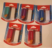 Five Maped retractable erasers each paired with a white refill eraser on red and blue backing cards, different colored plastic casings visible