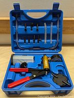 Blue plastic case opened to show all components organized for a brake bleeder and vacuum pump kit including the main pump, fluid reservoir, pressure gauge, several tubes, and adapter fittings.
