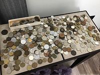 Overview of mixed coins spread across two tabletops with a small tray of coins