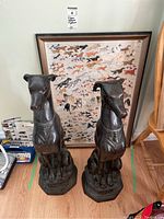 Front view of two dark metal seated dog statues and framed print behind