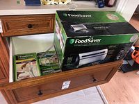 FoodSaver products in wooden drawer showing vacuum sealing bags and accessories, with large FoodSaver box stored above for vacuum sealing machine.
