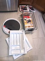 Overview of kitchen storage lot showing drawer organizers, metal wire basket with accessories, and packaging materials.