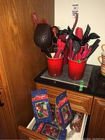 Two red Le Creuset utensil holders filled with assorted kitchen utensils along with potpourri bags below on a drawer.