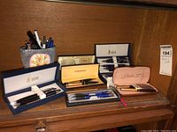 Overview of all vintage pen sets and individual pens on wooden shelf showing boxes and pen holder with loose pens.