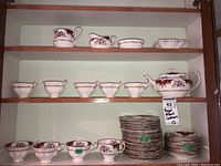 Overall view of three shelves displaying cups, serving pieces, stacks of plates