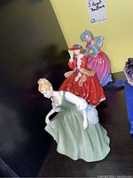 Three Royal Doulton figurines displayed together, showing different colored dresses and poses.