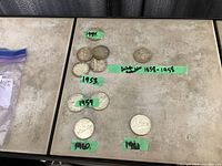 Ten silver dollar coins arranged with green tape labels indicating years 1951, 1953, 1959, 1960, 1961, plus a British Columbia Centennial coin.