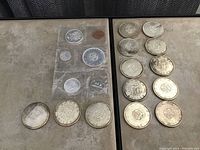 13 loose 1964 Canadian silver dollar coins arranged in rows beside a plastic sleeve containing additional 1964 coins
