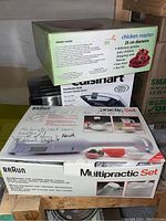 Photo showing stacked boxes of Braun Multipractic Set hand blender, chicken roaster, and Cuisinart sandwich grill