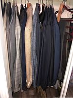 Nine men’s suit jackets hanging on wooden and plastic hangers in closet