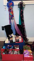 View of various scarves hanging and displayed, with packaged tights and other items inside a carry-on suitcase and a box in front.