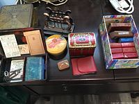 Overview of lot showing assorted vintage miniature books, various vintage tins including Bing Pygmyphone tin, playing cards, keys, and a bronze-tone letter holder on wooden surface.