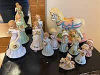 Overall set of Growing Up Birthday Girls figurines arranged with large pastel carousel horse on black surface.