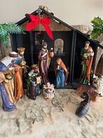 Full view of nativity set with black stable, red bow, and figurines arranged in front on marble surface