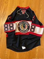 Full front view of black Chicago Blackhawks hockey jersey with #88 on sleeves and front logo.