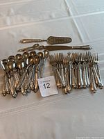 Full view of cutlery set on white cloth including forks, spoons, butter knife, and pie server