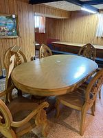 Full view of oval wooden dining table with 6 chairs around it in a wood-paneled room.