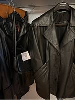 Two black leather jackets hanging on hangers, one with visible pockets and button closure, the other partially visible on a metal hanger with purse hung on the jacket's hanger