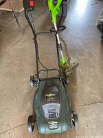 Yardworks electric lawn mower and Greenworks electric trimmer shown side-by-side on garage floor.