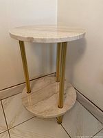 Side view of the two-tiered side table showing round marble tops and three gold metal legs.