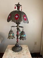 Full side view of one Victorian parlour lamp showing brass body, decorative shade with red jewel accents and hanging lamp shades