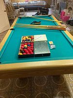 Pool table overview with cues, boxes of balls and triangle rack on green felt surface