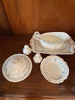 Full view of the bone china set displayed on wood surface showing all pieces including gravy bowl, butter dish, salt and pepper shakers, and plates