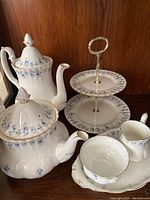 Full view of coffee pot, tea pot, dessert stand, creamer, sugar bowl and underplate arranged on wood surface.