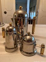 Front angle showing all three pieces of the stainless steel coffee set with gold-tone accents on lids and handles.