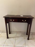 Full view of the dark wood console table showing two drawers with brass handles and straight legs on tiled floor against wall.