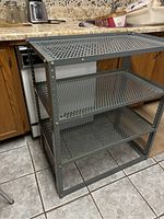 Gray metal shelving unit with three perforated shelves, shown next to kitchen cabinets and countertop.
