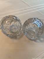 Two clear crystal ashtrays placed side by side on white fabric, showing overall shape and design.