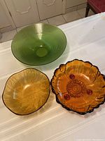 Three vintage glass bowls including a retro green bowl, a textured amber bowl, and a sunflower-shaped amber bowl with red accents.
