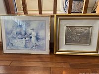 Two gold-framed artworks with 3-D silver embossed vintage prints, positioned side by side on a wooden floor.