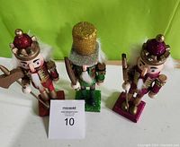 Three hand painted nutcracker figurines displayed upright on a white surface against a green background, showing front and side views.