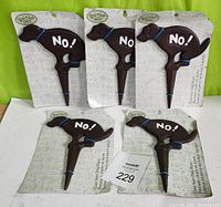 Five new cast iron garden signs shaped like dogs with 'NO!' written on the side, attached to white backing cards, displayed against a green background.
