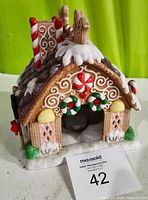 Front view of ceramic gingerbread house tea light holder showing detailed decorations including peppermint wreaths, candy canes, and window accents with snow-like icing.