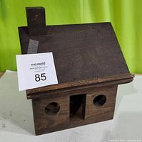Front and angled view of the brown wooden bird house showing the slanted roof, chimney detail, two circular entry holes and central rectangular opening.